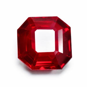 May include: A faceted, octagonal-cut, red gemstone with a square center. The gem is a vibrant, deep red color and appears to be highly polished. The gemstone is set against a white background, highlighting its brilliance and clarity.