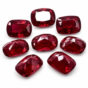 Könnte beinhalten: Eine Ansammlung von sieben losen Rubinen im Kissenschliff mit tiefroter Farbe und facettierten Oberflächen. Jeder Edelstein weist eine brillante, reflektierende Qualität mit scharfen Kanten und einer symmetrischen, abgerundeten Form auf.