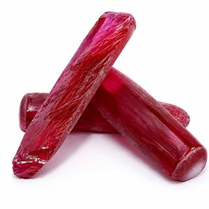 May include: Three elongated, cylindrical raw ruby crystals with a deep red color and a translucent, textured surface. The stones are arranged in a stacked formation, showcasing their natural, unpolished, and irregular crystalline structure.