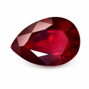 Könnte beinhalten: Ein facettierter, birnenförmiger Rubin-Edelstein. Der Edelstein hat eine tiefe, satte rote Farbe mit polierter Oberfläche. Die Facetten fangen das Licht ein und erzeugen Glanzlichter und Schatten. Der Edelstein ist vor einem weißen Hintergrund platziert.