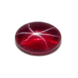 Puede incluir: Una gema pulida, de forma ovalada, de color rojo intenso, con un patrón de estrella de seis rayos. El efecto de estrella se crea por la luz que se refleja en las inclusiones dentro de la piedra. La gema está sobre un fondo blanco.