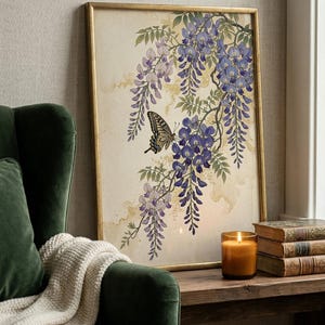 K&ouml;nnte beinhalten: Gerahmter Kunstdruck mit einem Schmetterling und Blauregenbl&uuml;ten in Lila und Blau. Das Kunstwerk befindet sich in einem goldenen Rahmen und steht auf einer Holzoberfl&auml;che neben einer brennenden Kerze und B&uuml;chern. Ein gr&uuml;ner Sessel ist im Vordergrund.