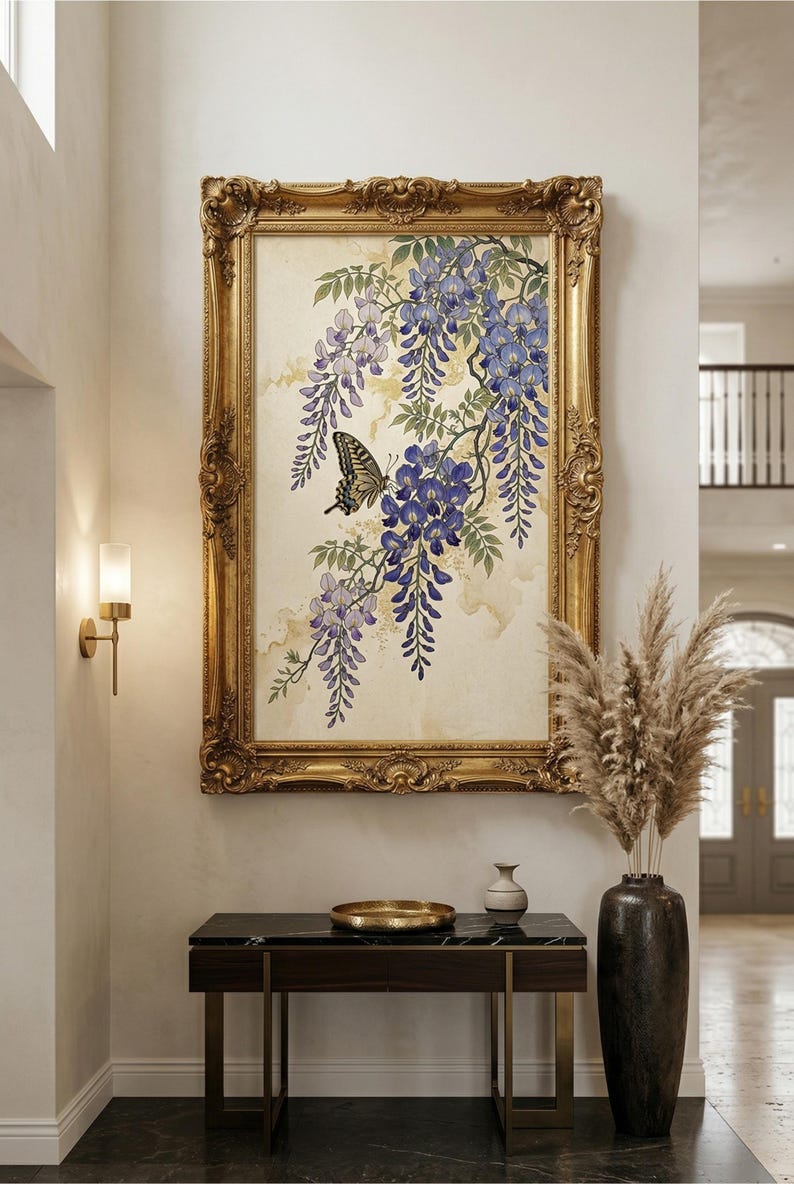 K&ouml;nnte beinhalten: Gerahmtes Kunstwerk mit einem Aquarellgem&auml;lde von Blauregenbl&uuml;ten in Lila und Gr&uuml;n, mit einem Schmetterling. Das Kunstwerk befindet sich in einem verzierten Goldrahmen, der &uuml;ber einem dunklen Holztisch mit einer goldenen Schale und Vase ausgestellt ist.