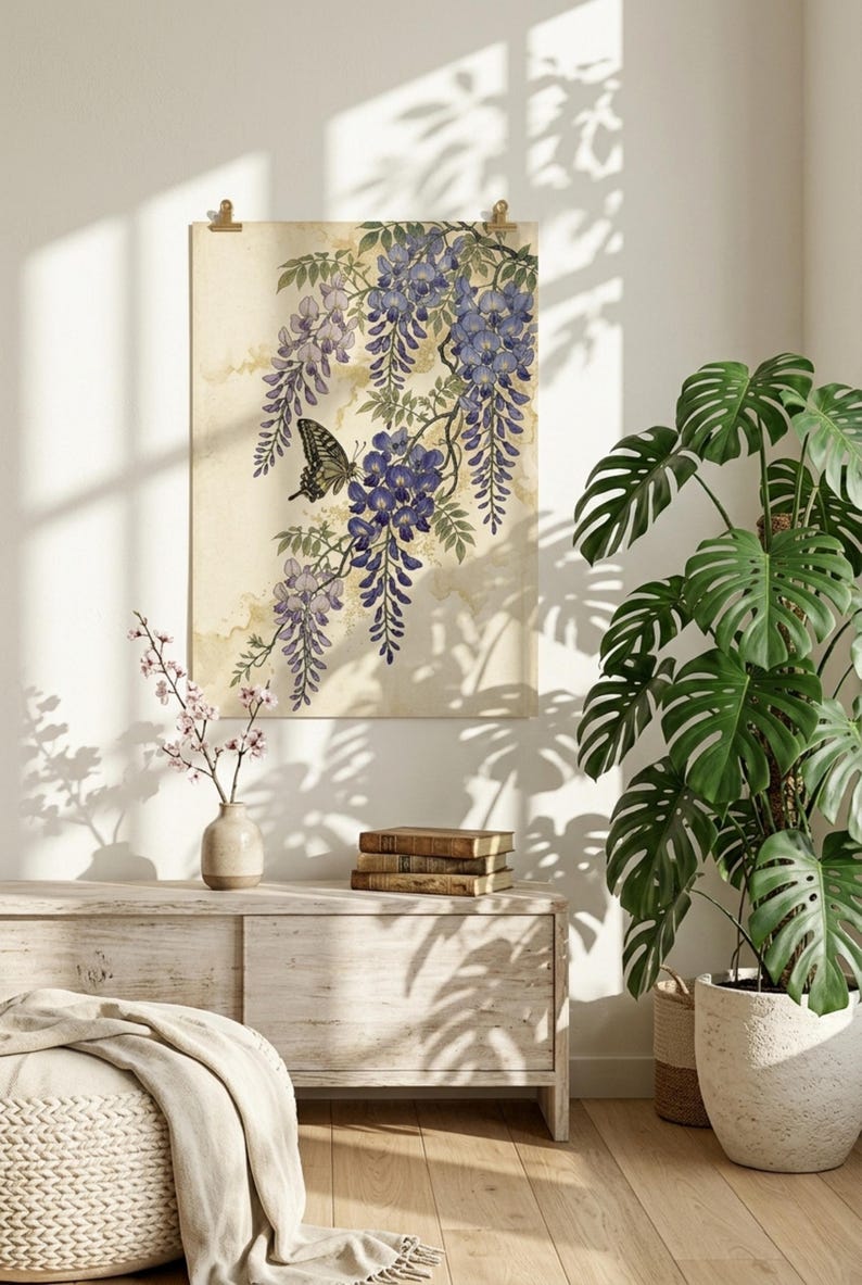 K&ouml;nnte beinhalten: Ein gerahmter Kunstdruck mit einer Aquarellillustration von Blauregenbl&uuml;ten und einem Schmetterling. Das Kunstwerk ist in Lila- und Gr&uuml;nt&ouml;nen gehalten, mit einem beigen Hintergrund. Der Druck h&auml;ngt &uuml;ber einem Holzschrank, mit einer Topfpflanze und B&uuml;chern.