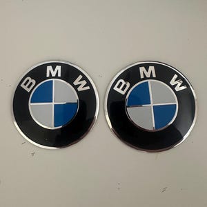 Può includere: Due emblemi circolari BMW caratterizzati da un anello esterno nero con le lettere bianche B, M e W. Il centro è diviso in quattro quadranti che si alternano tra blu e bianco, il tutto racchiuso da un sottile bordo metallico argentato.