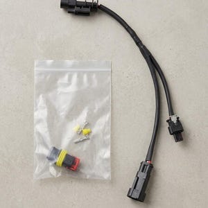 Pode incluir: Um chicote elétrico preto com design em Y e três conectores de plástico preto. Um saco plástico transparente contém pequenos terminais metálicos e um conector preto e vermelho com uma vedação de borracha amarela.