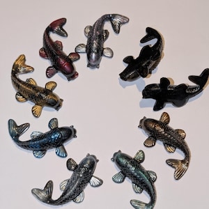 May include: A collection of decorative koi carp figurines in gold, black, silver, red and blue. The fish are arranged in a circle, displaying their detailed scales and fins. Each figurine is approximately 10 cm in length.