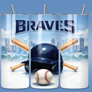 May include: A baseball-themed tumbler featuring the word "BRAVES" in navy blue, a navy blue helmet, a baseball, and two crossed bats. The background shows a cityscape under a blue sky with white clouds. The tumbler has a silver straw.