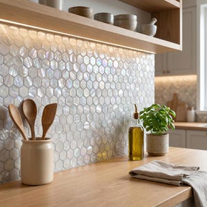 May include: A kitchen splashback featuring iridescent white hexagonal tiles with a pearlescent finish. The wall is illuminated by under-cabinet lighting, highlighting the reflective surface of the tiles above a wooden worktop with kitchen accessories.
