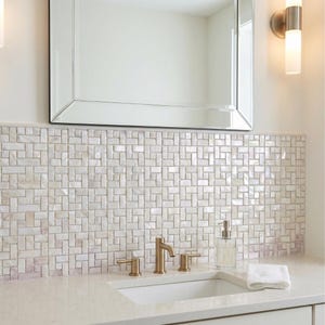May include: A bathroom vanity featuring a white rectangular undermount sink, a brushed gold faucet with two handles, and a white countertop. The wall is covered in a white iridescent mother-of-pearl mosaic tile backsplash with a basketweave pattern.