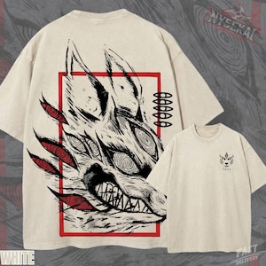 Könnte beinhalten: Cremefarbenes T-Shirt mit einer detaillierten schwarz-roten Wolfsillustration in einem roten Rahmen. Das Design zeigt scharfe Zähne und mehrere Augen. Auf der Vorderseite befindet sich ein kleineres Wolfskopf-Motiv.
