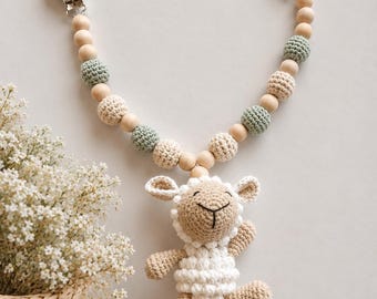 Op de afbeelding: Een speenkoord met een gehaakt wit en beige lammetje, bevestigd aan een koord van afwisselende houten kralen en saliegroene en crèmekleurige gehaakte bollen, afgewerkt met twee ronde houten clips aan de uiteinden van het koord.