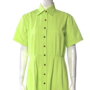 May include: A lime green midi dress with short sleeves and a button-down front. The dress features a collared neckline and a fitted waist. The buttons are a dark brown color. The dress is displayed on a mannequin.