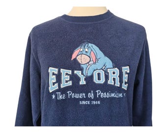 May include: A navy blue fleece sweatshirt with a blue Eeyore character graphic and the text "Eeyore The Power of Pessimism Since 1966".