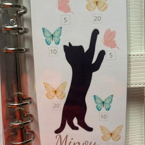 May include: A white rectangular card insert for a binder featuring a black silhouette of a cat reaching upward. The card is decorated with colorful butterflies in shades of pink, blue, and yellow, each paired with a number: 5, 10, or 20. The word Minou is printed in a cursive script at the bottom.