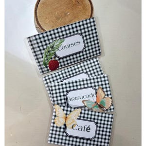 May include: Three rectangular labels with a black and white gingham pattern. The top label features a green sprig and a red raspberry with the text Courses. The middle label shows a butterfly with the text Brasucade. The bottom label displays a yellow butterfly with the text Café.