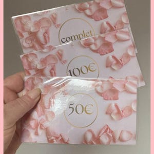 Peut inclure: Trois cartes cadeaux avec un motif floral de pétales de roses roses. Les cartes portent des inscriptions dorées : "complet", "100€" et "50€". Les cartes sont dans des pochettes en plastique transparent.