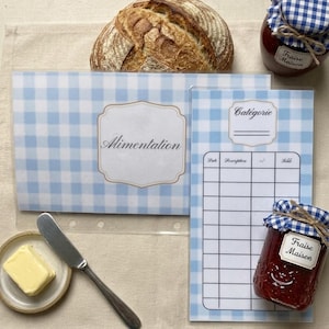 Peut inclure: Nature morte avec un pain rustique, deux pots de confiture, un couteau à beurre et une petite assiette de beurre. La scène comprend un dossier à carreaux bleu et blanc et un bloc-notes avec les mots "Alimentation" et "Categorie".