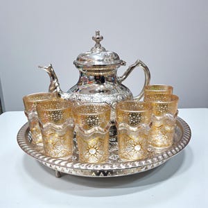 Puede incluir: Una taza de cerámica blanca con un asa negra y el texto "But First, Coffee" en negro, con una fuente de estilo manuscrito. La taza está sobre una superficie blanca.