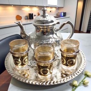 Könnte beinhalten: Eine weiße Keramik-Tasse mit schwarzem Henkel und dem Text "But First, Coffee" in schwarzer, handschriftlicher Schrift. Die Tasse steht auf einer weißen Oberfläche.