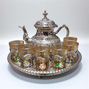Könnte beinhalten: Ein silbernes Teeservice mit einer Teekanne und sechs Gläsern, alles auf einem silbernen Tablett. Die Gläser haben ein goldenes Filigranmuster mit roten, blauen und grünen floralen Akzenten. Die Teekanne ist aufwendig verziert.
