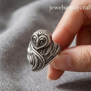 May include: A silver owl ring with detailed carving. The ring depicts an owl with intricate feather and eye detailing. The ring is held by a hand. The text "jewelsemilycraft" is visible in the background.