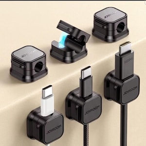 Pode incluir: Organizadores de cabos pretos com o logotipo "JOYROOM", segurando vários tipos de cabos, incluindo USB-C e HDMI. Alguns organizadores estão abertos, outros fechados. Os organizadores são quadrados com um topo prateado.
