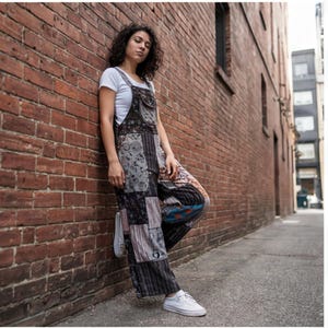 May include: A pair of patchwork overalls featuring a variety of dark-toned fabric patterns including floral, striped, and abstract designs, worn over a plain white short-sleeved t-shirt with white low-top sneakers to complete the outfit.