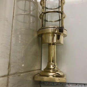 May include: A brass-colored, vintage-style lamp with a clear glass enclosure. The lamp features a cylindrical design with a protective cage and a sturdy base. The lamp measures approximately 14 inches in height.
