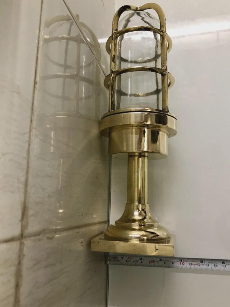 May include: A brass-colored, vintage-style lamp with a clear glass enclosure. The lamp features a cylindrical design with a protective cage and a sturdy base. The lamp measures approximately 14 inches in height.