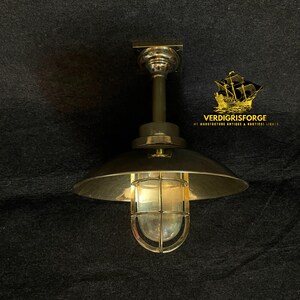May include: A brass-toned ceiling light fixture with a domed shade and a caged glass enclosure. The fixture has a nautical or industrial design, with the text "VERDIGRISFORGE" and a ship logo visible.