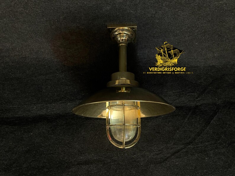 May include: A brass-toned ceiling light fixture with a domed shade and a caged glass enclosure. The fixture has a nautical or industrial design, with the text "VERDIGRISFORGE" and a ship logo visible.