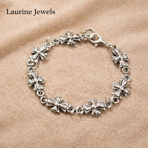 May include: A silver bracelet with decorative cross-shaped links. The bracelet has a lobster clasp. The brand name "Laurine Jewels" is visible. The bracelet is displayed on a neutral-toned surface. The bracelet's links are approximately 1.5 cm in size.
