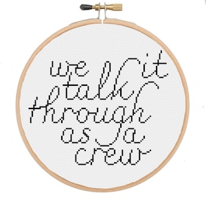 Op de afbeelding: Een borduurring met kruissteek met de woorden "we walk it talk through as a crew" in zwart schrift. De tekst is geborduurd op witte stof en omlijst door een natuurlijke houten ring.