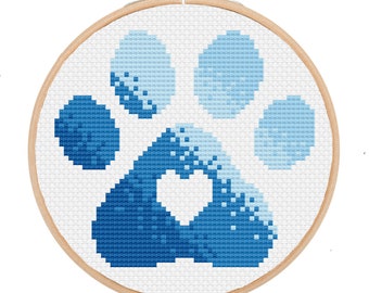 May include: A blue and white paw print with a heart in the center, embroidered on white fabric in a round wooden embroidery hoop.