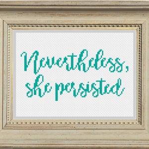 May include: A framed cross-stitch with the text "Nevertheless, she persisted" in teal lettering on a white background.