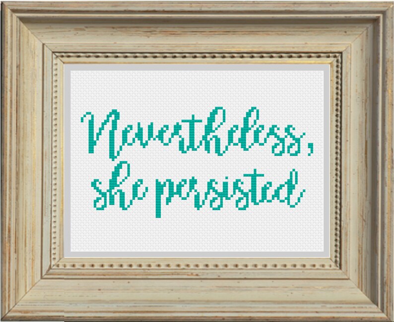 May include: A framed cross-stitch with the text "Nevertheless, she persisted" in teal lettering on a white background.