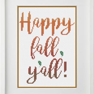 May include: Cross stitch pattern with the text "Happy fall y'all!" in a gradient of orange and red. The text is in a cursive font and there are small green leaves scattered around the text.