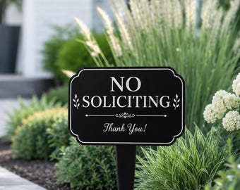 May include: A black rectangular garden sign with rounded corners and a white border. The sign features the white text NO SOLICITING, a decorative horizontal line, and the text Thank You! with small leaf icons on either side of the main text.