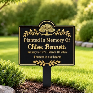 May include: Black and gold memorial garden stake. The rectangular sign reads "Planted In Memory Of Chloe Bennett" with dates and "Forever in our hearts." A tree and leaf design adorns the top and bottom.