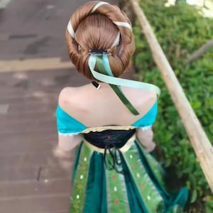 May include: A dress featuring a black bodice with gold trim and a dark green skirt with vertical panels decorated with small white and red floral patterns. The hair is styled in a large, rounded bun with a light green ribbon tied around the base.