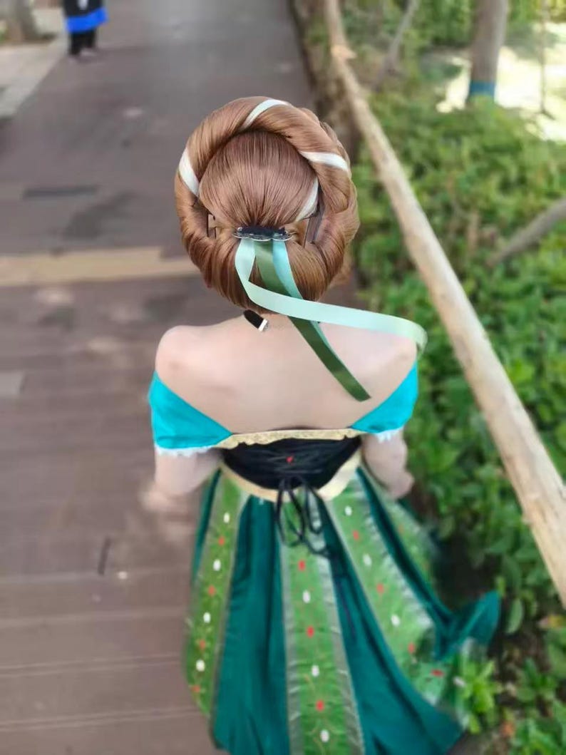 May include: A dress featuring a black bodice with gold trim and a dark green skirt with vertical panels decorated with small white and red floral patterns. The hair is styled in a large, rounded bun with a light green ribbon tied around the base.