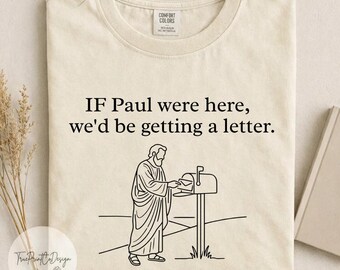 Può includere: Una t-shirt color crema a girocollo con un disegno a linee nere di una persona in tunica che inserisce una lettera in una cassetta postale. Il testo sopra la grafica recita: IF Paul were here, we'd be getting a letter. La maglia ha un'etichetta.