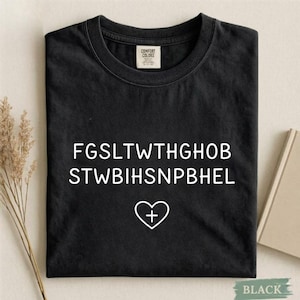 Könnte beinhalten: Schwarzes T-Shirt mit weißem Text und einem Herz mit einem Kreuzsymbol. Das T-Shirt hat einen Rundhalsausschnitt und ein Etikett mit der Aufschrift "Comfort Colors". Der Text auf dem T-Shirt ist in einem kryptischen Format.