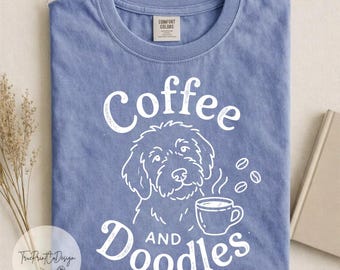 Può includere: Una t-shirt a maniche corte color blu pervinca con una stampa grafica bianca raffigurante il muso di un cane e una tazza di caffè. Il testo recita Coffee AND Doodles. La maglietta presenta un girocollo e un'etichetta Comfort Colors.