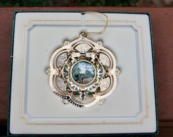 May include: A gold-colored Christmas ornament with a white and green design. The ornament features a small image of the White House with the text "White House" above it.