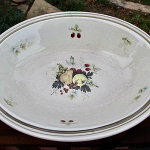May include: Oval ceramic serving platter with a cream-colored base and a decorative fruit and leaf design. The rim features two olive green stripes. The platter is decorated with images of pears, grapes, and berries.