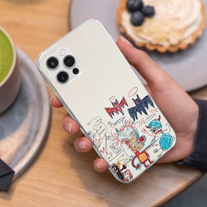 May include: Clear phone case with a colorful, abstract doodle design. The artwork features red, blue, and yellow figures, bats, and scribbled lines. The case is held in a hand, with a blurred background.