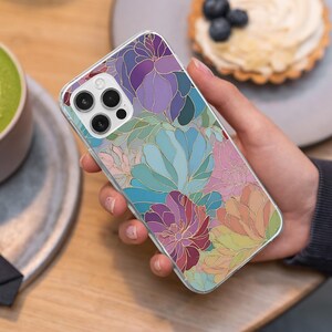May include: A clear phone case featuring a floral design with purple, blue, pink, and gold accents. The case is held in a hand, showcasing the colorful pattern. The design includes various flower shapes.