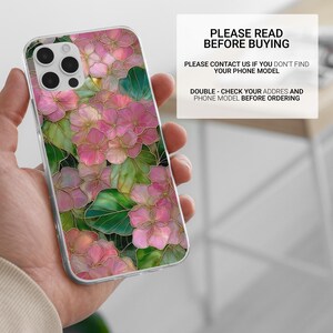 May include: A clear phone case featuring a floral design with pink and green flowers and gold outlines. The case has the text "PLEASE READ BEFORE BUYING" and other instructions. The phone case is held in a hand.